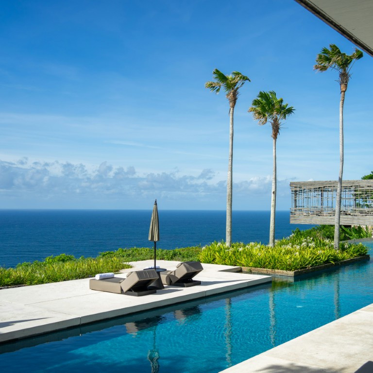 a pool with a lounge chair and umbrella by a body of water